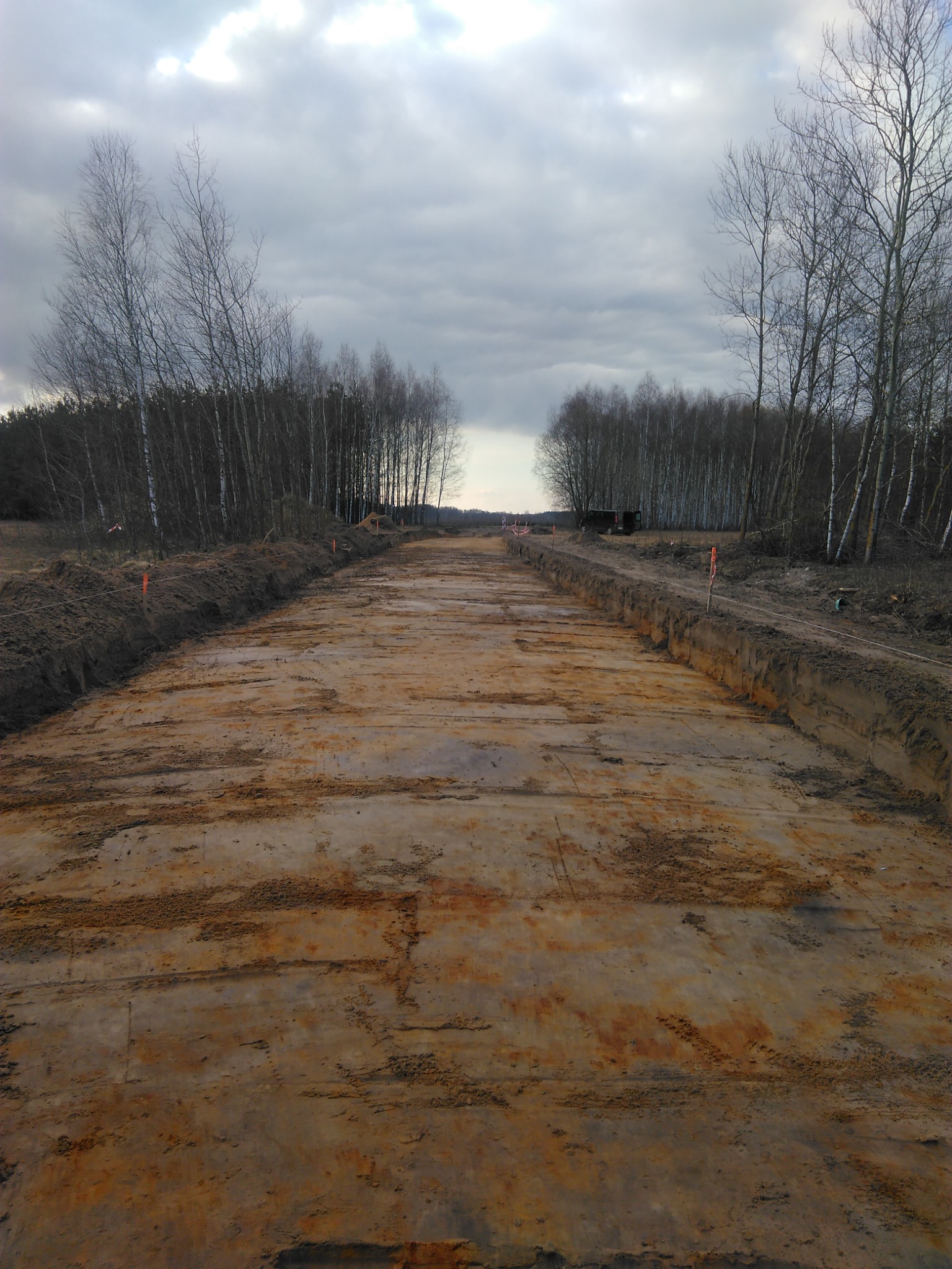 Przygotowany teren pod budowę drogi, widoczne wytyczone krawędzie i wyrównana powierzchnia gruntu, drzewa w tle.