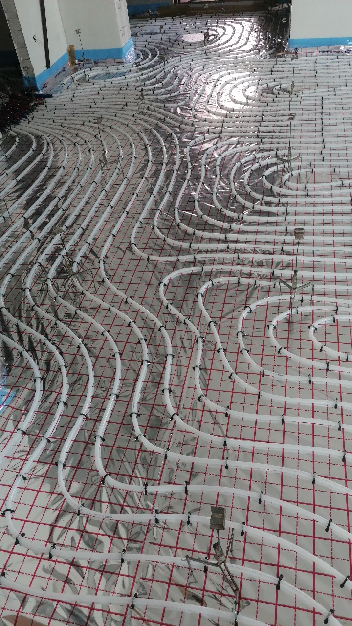 Rozłożone rury ogrzewania podłogowego na folii z siatką, zabezpieczone klipsami, widok z góry na dużą powierzchnię w trakcie montażu.