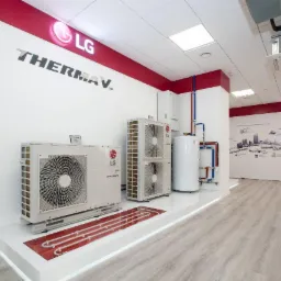 Wnętrze salonu z ekspozycją systemów klimatyzacji i ogrzewania LG Therma V, obejmującą jednostki zewnętrzne, wewnętrzne oraz zasobnik ciepłej wody, z widocznym schematem ogrzewania podłogowego...