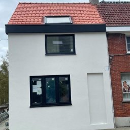 Łukasz Olesiński Usługi Budowlane - Dom z nową, czerwoną dachówką, oknem dachowym i czarną obróbką blacharską, przylegający do budynku z cegły.