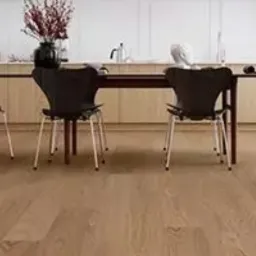 Jasna, drewniana podłoga w jadalni z trzema czarnymi krzesłami o metalowych nogach ustawionymi wokół ciemnego stołu; w tle białe ściany i jasne szafki kuchenne z dekoracjami.