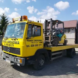 Żółta laweta z napisem 'Pomoc Drogowa' przewozi wózek widłowy Komatsu na platformie. Widoczne numery telefonów i rejestracja pojazdu.