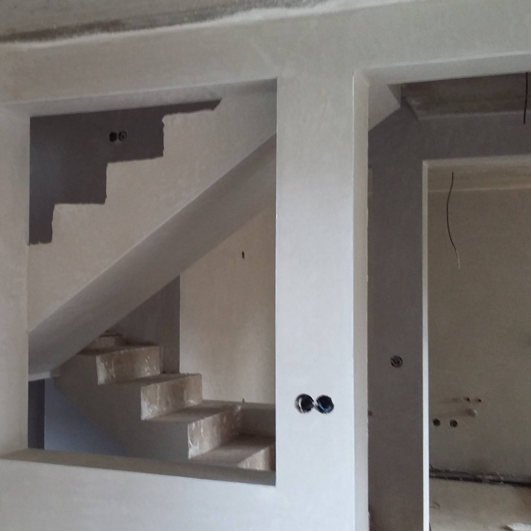 Surowe schody z widocznymi stopniami w trakcie tynkowania maszynowego, z widocznymi puszkami elektrycznymi w ścianie