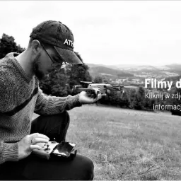 Operator drona w czapce ATH przygotowuje się do lotu na tle pagórkowatego krajobrazu. Kontroler drona spoczywa na jego kolanach.