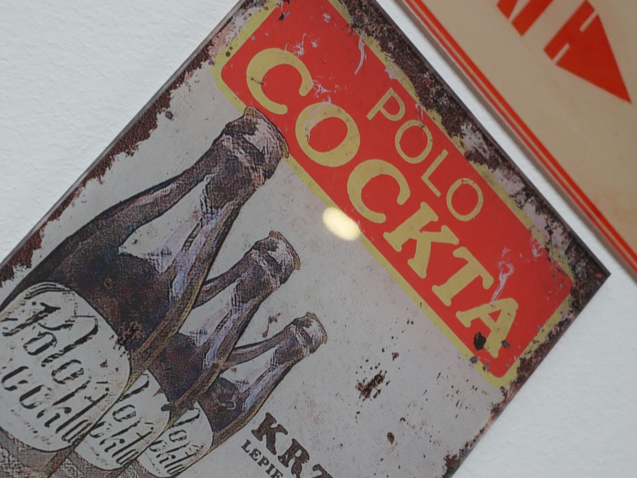 Metalowa tablica reklamowa w stylu retro z napisem 'Polo Cockta' i wizerunkiem butelek, z widocznymi śladami rdzy i zużycia.
