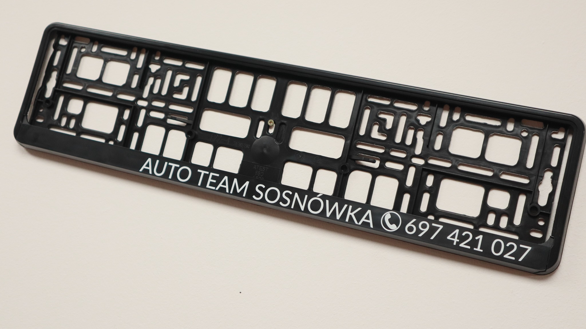 Czarna ramka pod tablicę rejestracyjną z białym nadrukiem 'AUTO TEAM SOSNÓWKA' i numerem telefonu na jasnym tle.