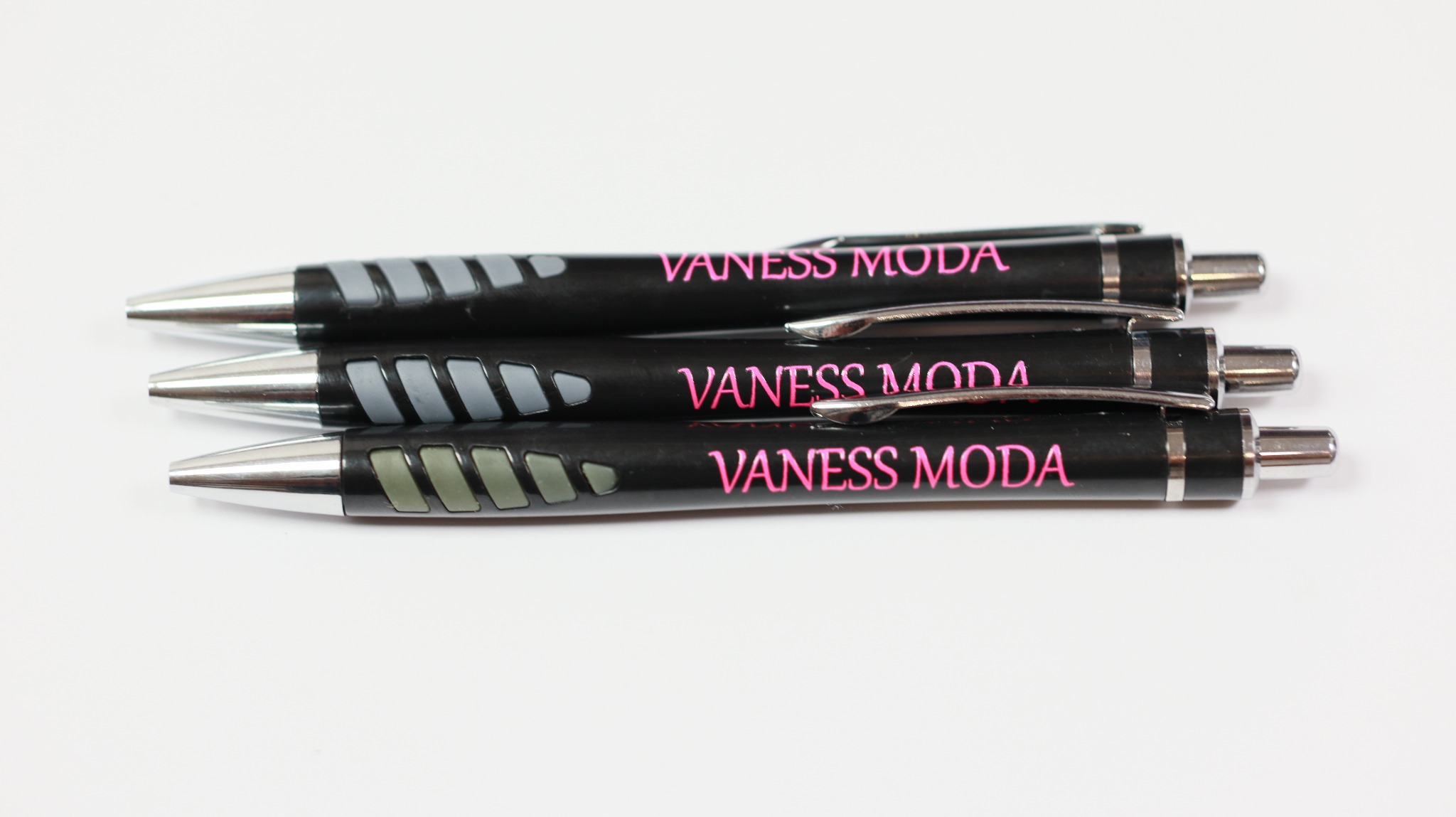 Trzy czarne długopisy z nadrukowanym różowym napisem VANESS MODA, ułożone równolegle na białym tle.