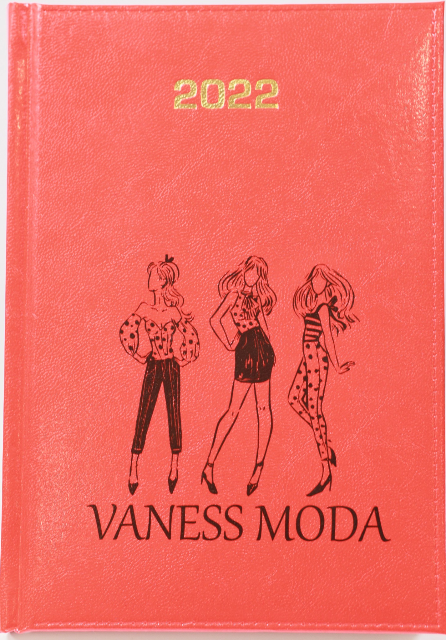 Czerwony kalendarz na rok 2022 z nadrukowanymi sylwetkami trzech kobiet w różnych stylizacjach i napisem VANESS MODA.