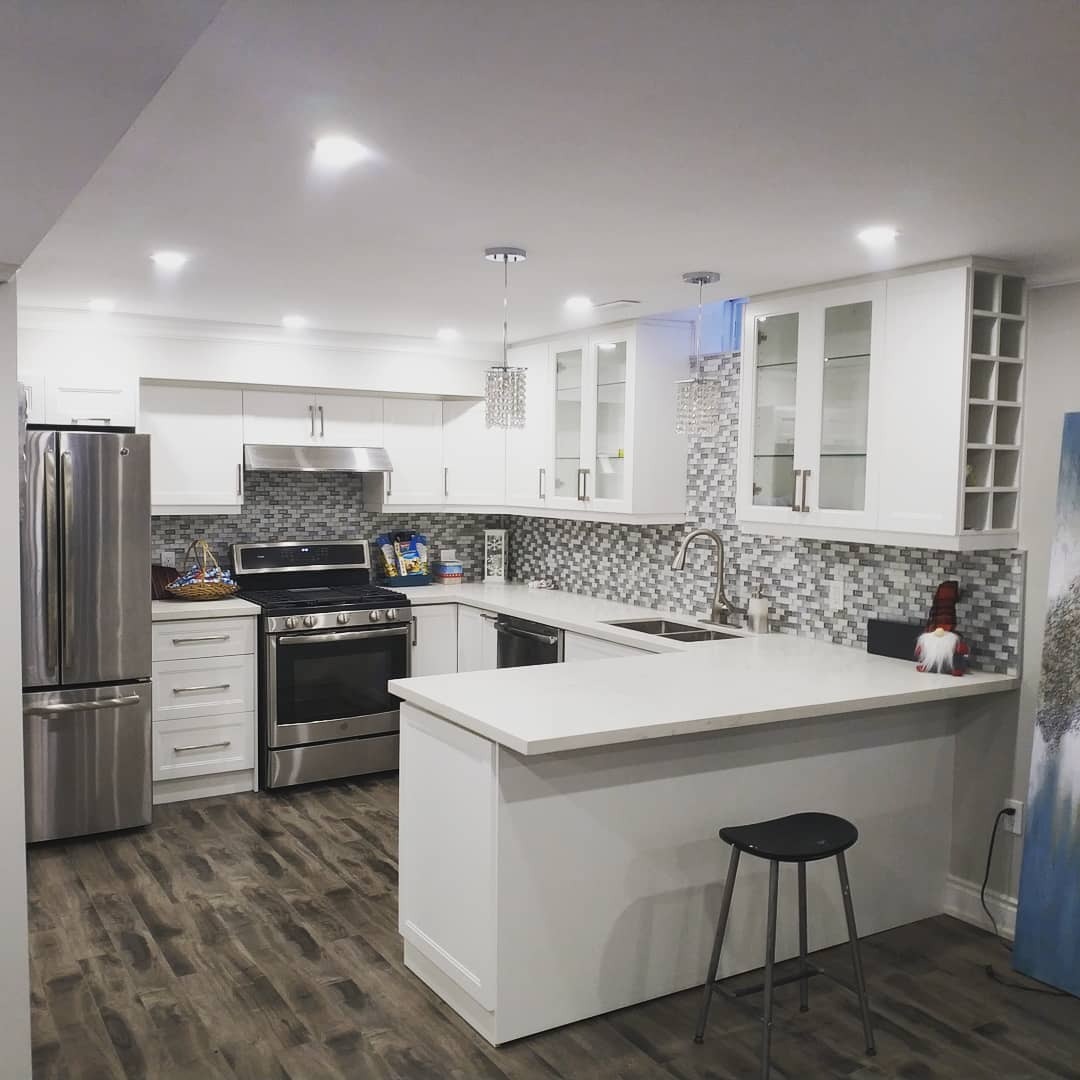 Wnętrze nowoczesnej kuchni z białymi szafkami, mozaikową ścianą nad blatem, stalową lodówką i piekarnikiem oraz drewnianą podłogą.