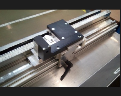 Precyzyjny mechanizm z czarnym modułem i srebrnymi prowadnicami, z miarką w tle, ukazujący detale narzędzia używanego w projektowaniu CAD/CAM.