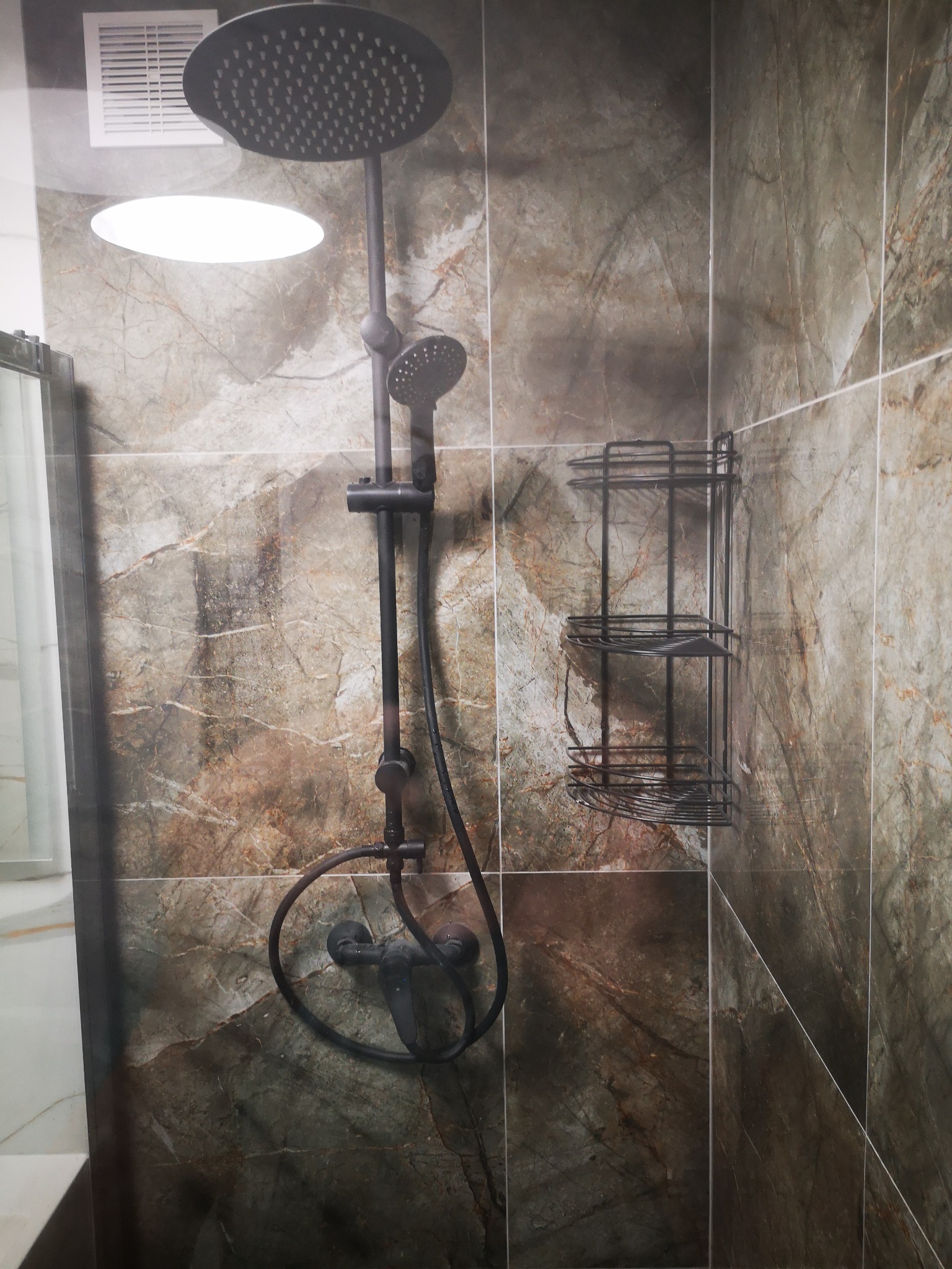 Czarny zestaw prysznicowy z deszczownicą i półka łazienkowa na marmurowych płytkach w kabinie prysznicowej.