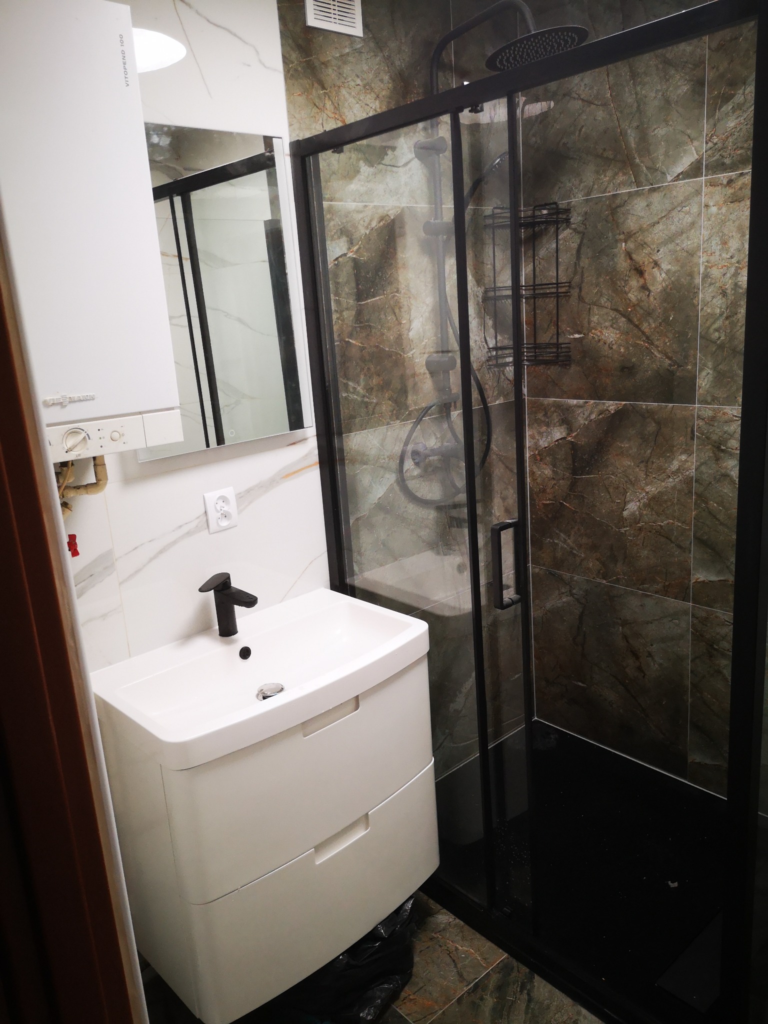 Nowoczesna łazienka z białą szafką umywalkową z czarną armaturą, kabiną prysznicową z czarnymi profilami i marmurowymi płytkami na ścianach.