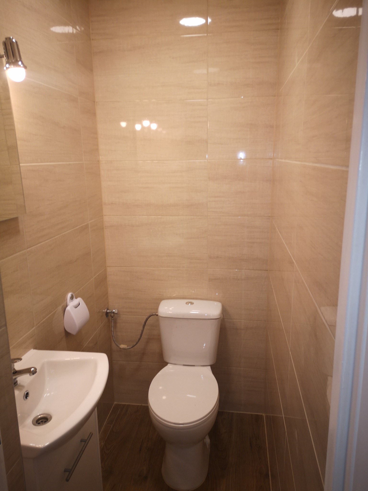 Wykończona łazienka w Gorzowie Wielkopolskim z beżowymi płytkami imitującymi drewno na ścianach i podłodze, biała umywalka z szafką i toaleta. Widoczny minimalistyczny dozownik papieru toaletowego.