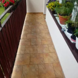 Balkon z brązowymi płytkami podłogowymi, drewnianą balustradą, kwiatami w skrzynkach i doniczkach, widok z góry.