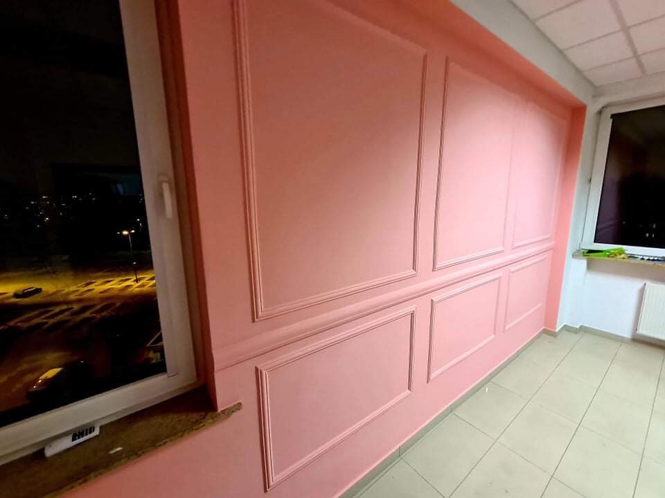 Różowa ściana z dekoracyjnymi panelami w mieszkaniu, widok na nocne miasto przez okno.