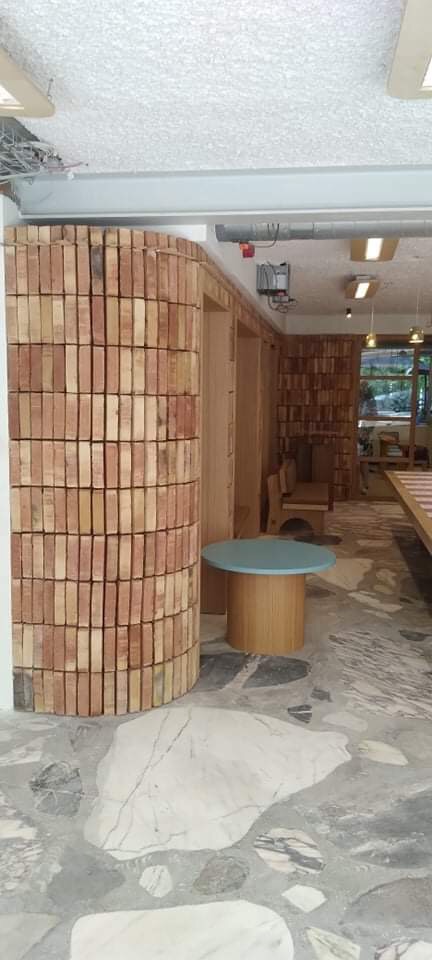 Cylindryczna ściana z cegieł w surowym wnętrzu, obok okrągły stolik z jasnoniebieskim blatem, posadzka z dużych kamiennych płyt.