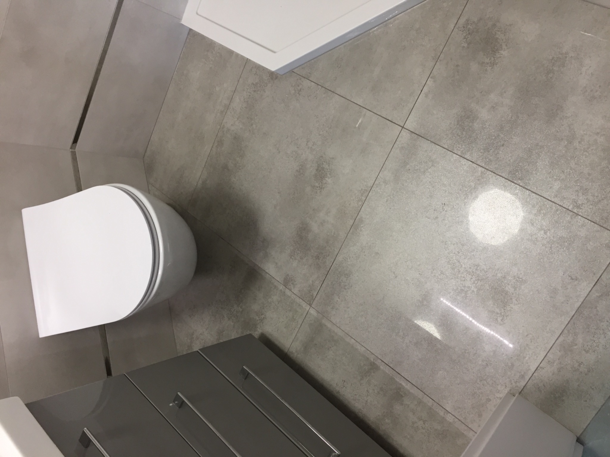 Nowoczesna łazienka z szarą płytką podłogową, wiszącą toaletą i szarą szafką pod umywalką, widok z góry.