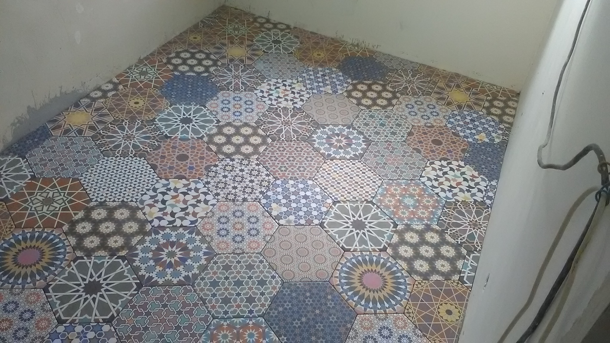 Ułożona podłoga z heksagonalnych płytek o wzorach marokańskich w odcieniach beżu, brązu i błękitu. Widoczne fragmenty ścian w surowym stanie.
