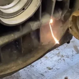 Czyszczenie elementu silnika metodą piaskowania, widoczny strumień piasku i dysza.