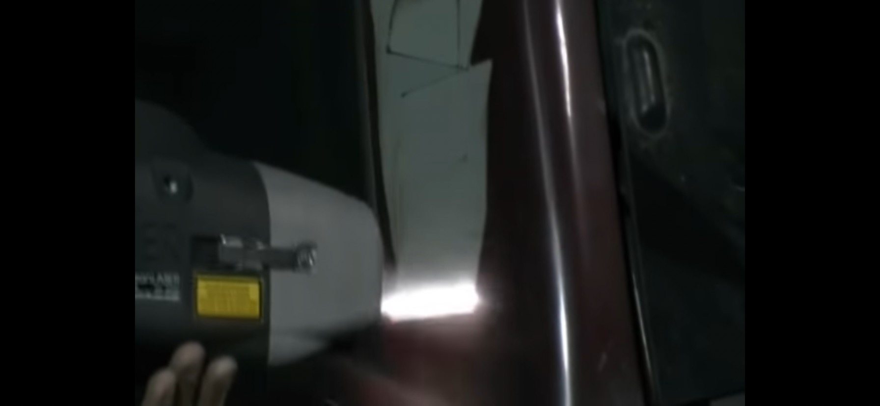 Aplikacja urządzenia do usuwania zadrapań na karoserii samochodu, widoczny fragment karoserii i ręka obsługująca urządzenie.