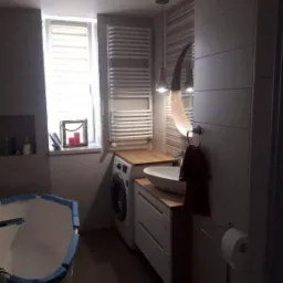 Nowoczesna łazienka z pralką obok umywalki na drewnianym blacie, grzejnik drabinkowy, okrągłe lustro z podświetleniem i wisząca lampa