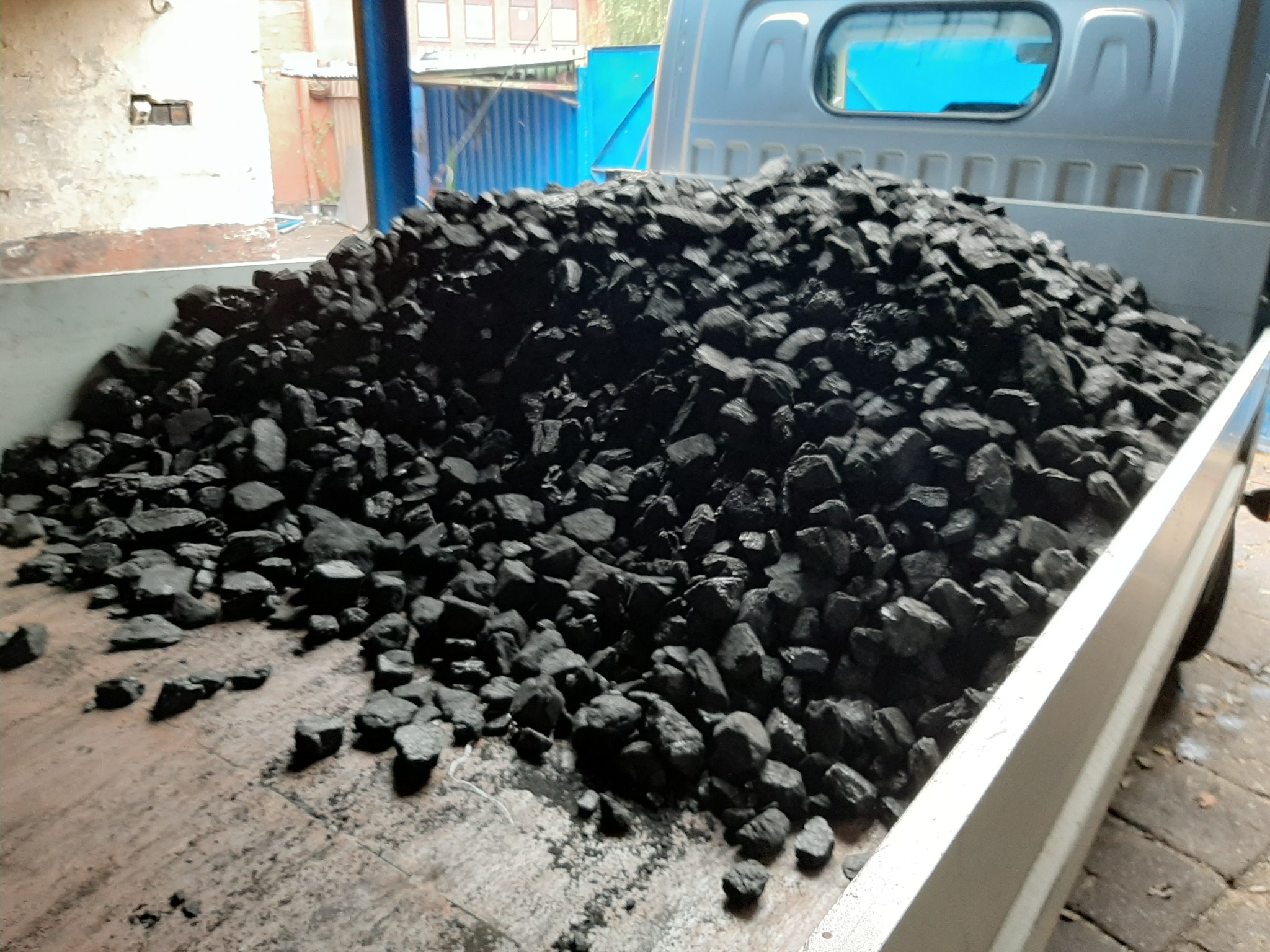 Ładunek węgla kamiennego w skrzyni transportowej samochodu dostawczego, z widocznymi bryłami na krawędzi skrzyni i zabrudzeniami po węglu.