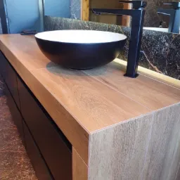 Nowoczesna łazienka w Pisarzowicach: czarna umywalka nablatowa i bateria na blacie z drewnopodobnych płytek, marmurowe wykończenie ściany w tle.