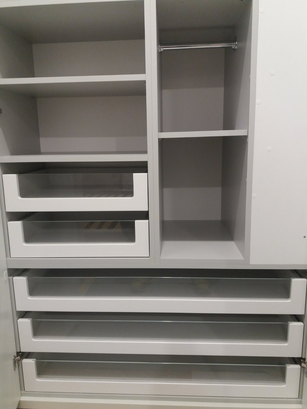 Wnętrze szafy z szufladami z frontami z przezroczystego szkła i półkami w jasnym odcieniu szarości, widoczny drążek na ubrania.