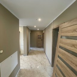 VDA REMONTY SPÓŁKA Z OGRANICZONĄ ODPOWIEDZIALNOŚCIĄ - Korytarz w trakcie remontu z marmurową podłogą, beżowymi ścianami i częściowo zamontowanymi drzwiami z drewnopodobnym fornirem i szklanymi wstawkami.