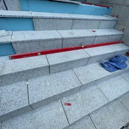 VDA REMONTY SPÓŁKA Z OGRANICZONĄ ODPOWIEDZIALNOŚCIĄ - Granitowe schody zewnętrzne w trakcie układania, poziomica, krzyżyki dystansowe, niebieska izolacja termiczna, widok z góry.