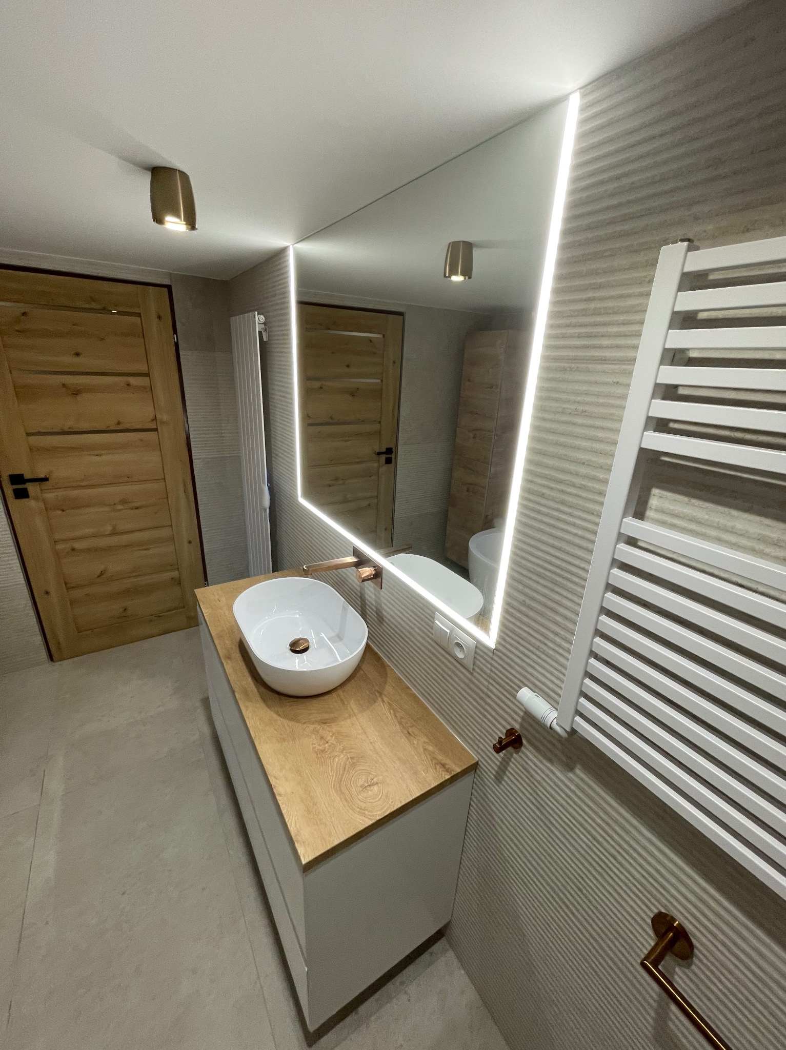 Nowoczesna łazienka z umywalką nablatową, podświetlanym lustrem, grzejnikiem drabinkowym i drewnianymi akcentami, widok z góry.