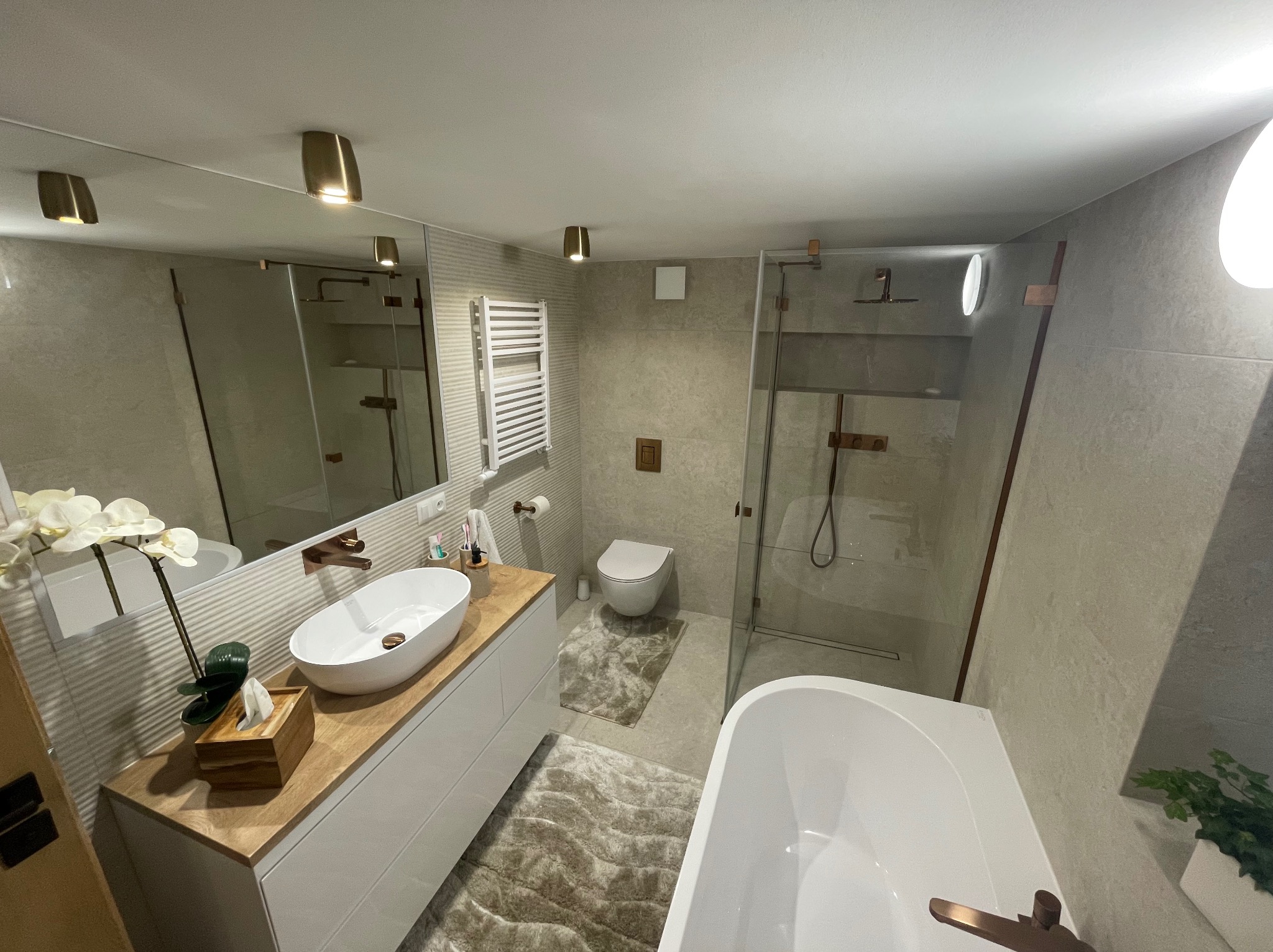 Nowoczesna, jasna łazienka w Katowicach z owalną umywalką nablatową, białą wanną, kabiną prysznicową ze szklanymi drzwiami i beżowymi płytkami na ścianach.