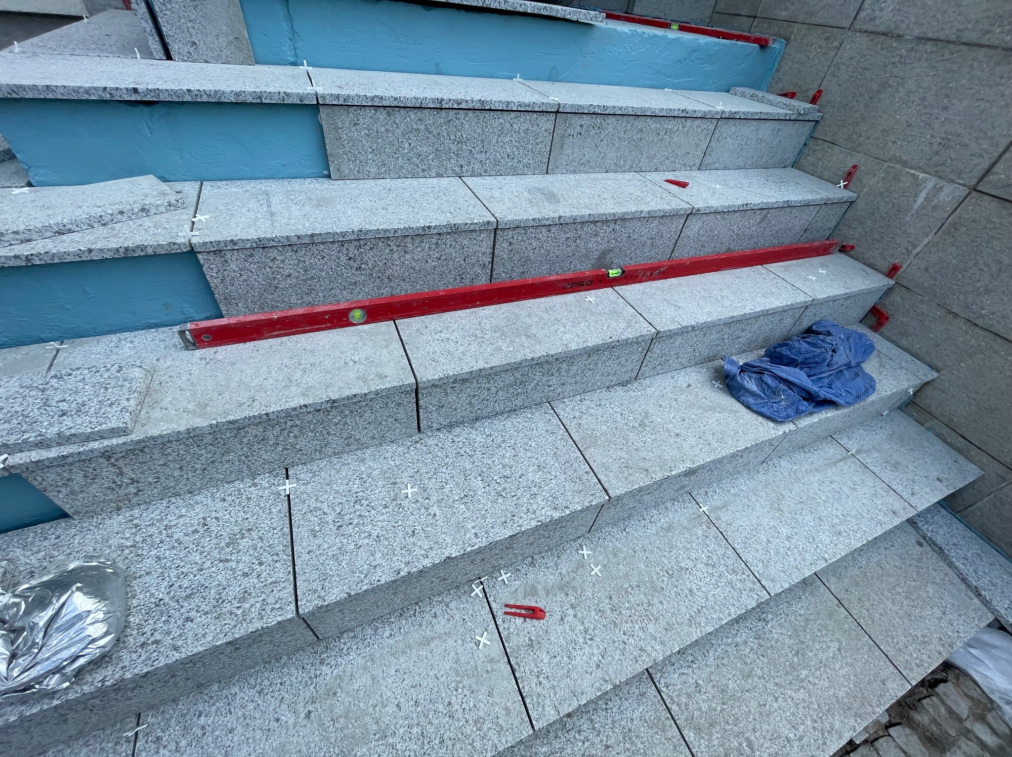 Granitowe schody zewnętrzne w trakcie układania, poziomica, krzyżyki dystansowe, niebieska izolacja termiczna, widok z góry.