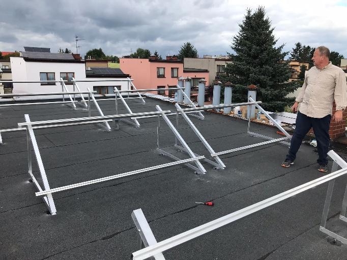 Montaż konstrukcji wsporczej pod panele na dachu pokrytym papą, widoczny pracownik w koszuli w paski i śrubokręt leżący na dachu.