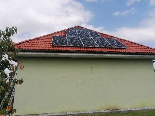 Panele fotowoltaiczne zamontowane na dachu domu z czerwoną dachówką, widok z dołu, drabina oparta o ścianę budynku.