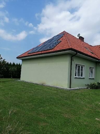 Zainstalowane panele słoneczne na czerwonym dachu domu jednorodzinnego, widok z poziomu trawnika w słoneczny dzień.