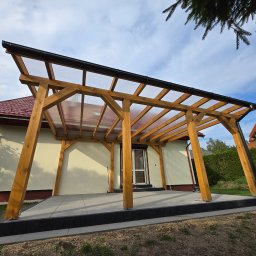 STOL-DACH MARCIN GRABOWSKI - Drewniana altana z przezroczystym zadaszeniem, przylegająca do domu z czerwonym dachem. Widoczne szare płytki tarasowe i zielony trawnik. Ujęcie z dołu, niebo z chmurami w tle.