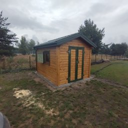 STOL-DACH MARCIN GRABOWSKI - Drewniana altana ogrodowa z zielonymi akcentami, widoczna z boku na tle pochmurnego nieba i drzew. Świeże ślady montażu na ziemi.