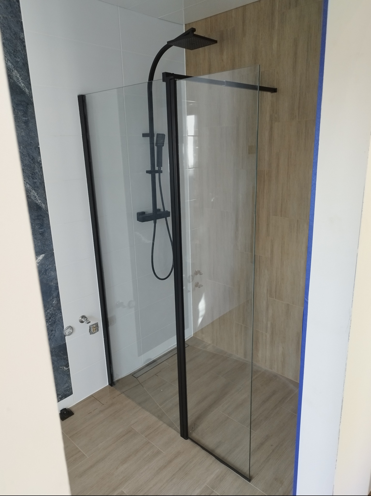 Nowoczesna kabina prysznicowa z czarnymi profilami i deszczownicą, wykończona płytkami w odcieniach bieli i beżu. Minimalistyczny design, widok z góry.