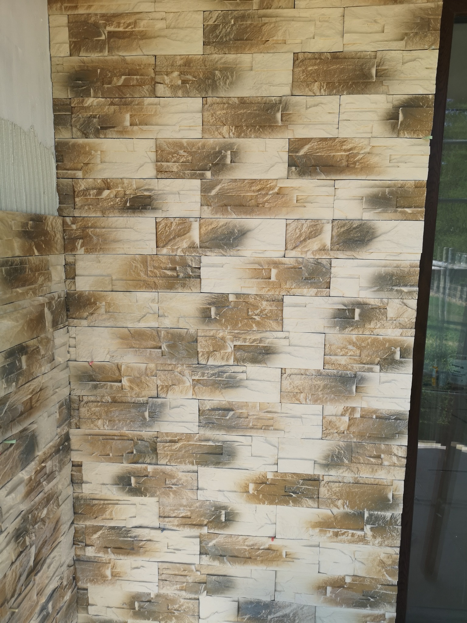 Ściana wyłożona panelami imitującymi kamień, z widocznym fragmentem ściany w trakcie prac wykończeniowych, gdzie widać nałożony klej.