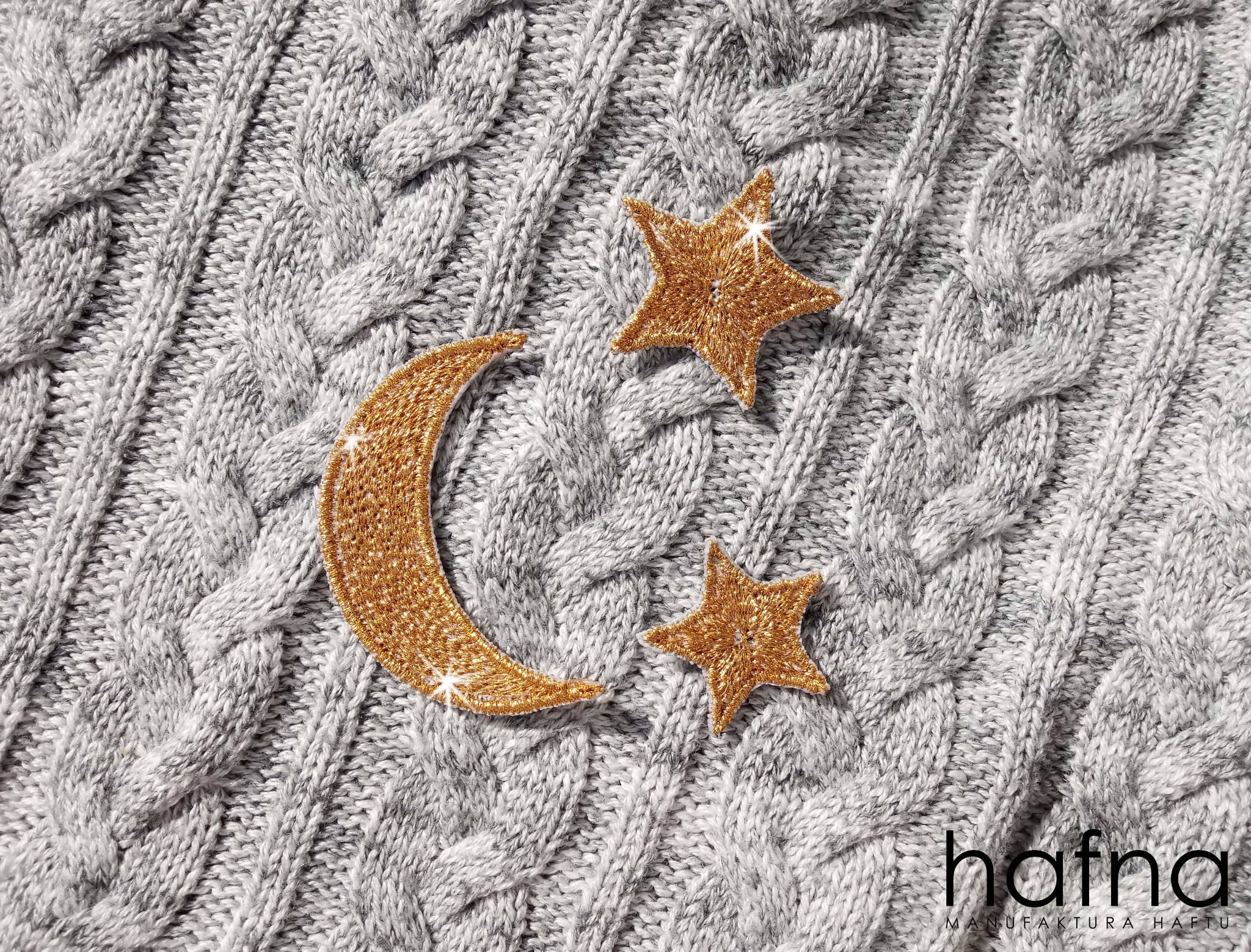 Szary sweter z warkoczowym splotem z haftowanymi złotymi gwiazdami i księżycem oraz logo firmy hafna