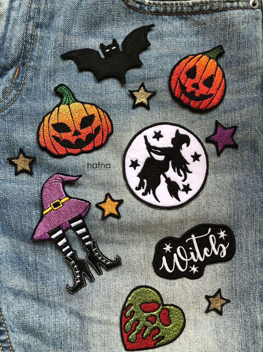 Dżinsowa tkanina ozdobiona naszywkami o tematyce Halloween: dynie z wyhaftowanymi twarzami, nietoperz, wiedźma na miotle, serce z zieloną czaszką, kapelusz i nogi wiedźmy oraz napisy i gwiazdki.