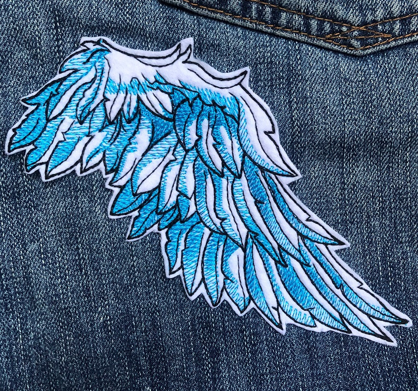 Niebiesko-białe skrzydło anioła, naszywka na dżinsowej kurtce, widoczny fragment kieszeni.