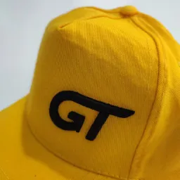 Żółta czapka z daszkiem z czarnym, haftowanym logo 'GT' na białym tle.