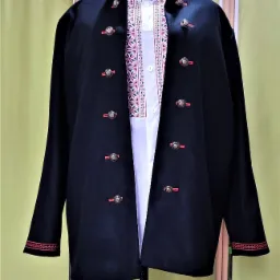 Czarny, wełniany żakiet z ozdobnymi guzikami i haftowanym wykończeniem na manekinie krawieckim, widoczna biała koszula z ludowym haftem.