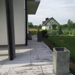 KAMSTEN kamieniarstwo budowlane - Nowoczesny taras z jasnych płyt kamiennych z minimalistycznymi donicami, widok na dom i ogród z zielonym trawnikiem.