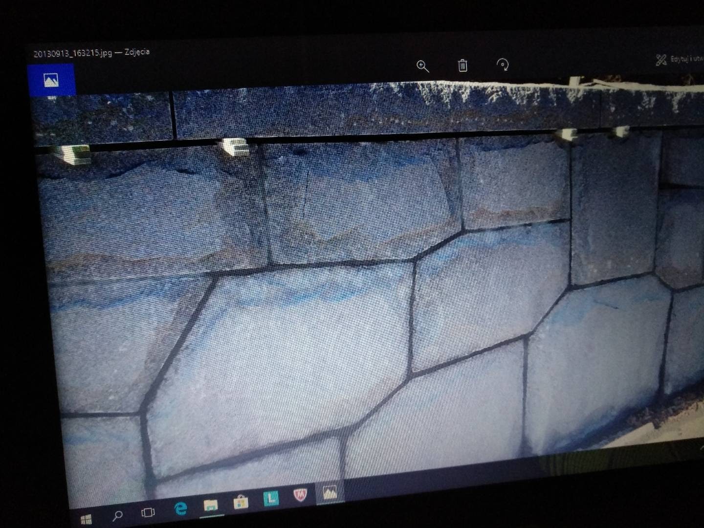 Fragment ściany wyłożonej nieregularnymi, szarymi kamieniami z widocznymi spoinami, sfotografowany z bliska pod kątem.