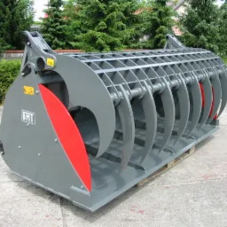 Szary, metalowy chwytak rolniczy z czerwonymi elementami na palecie, widok z boku na tle zieleni.