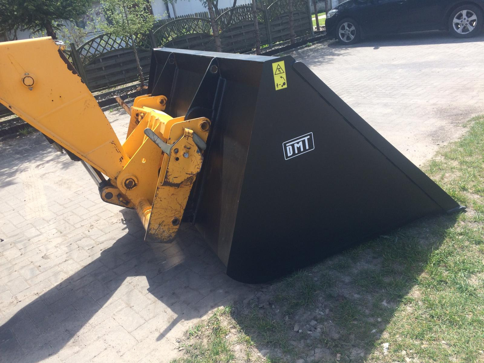 Czarny, stalowy osprzęt koparki z żółtym ramieniem montażowym, widoczne ślady użytkowania i logo DMT.