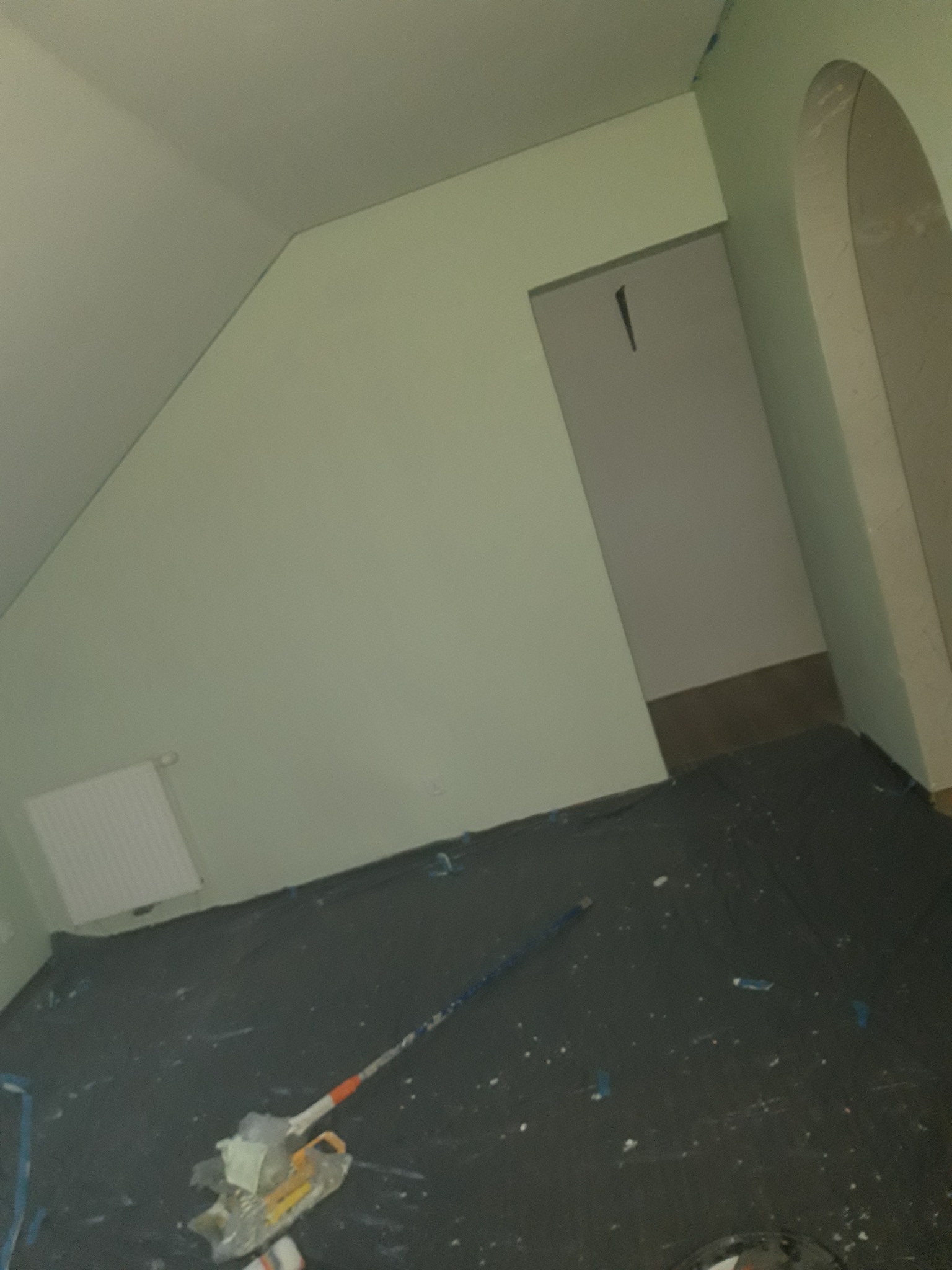 Pokój w trakcie odświeżania, widoczne pomalowane na jasnozielono ściany, zabezpieczona folią podłoga, grzejnik oraz wałek malarski z kuwetą.